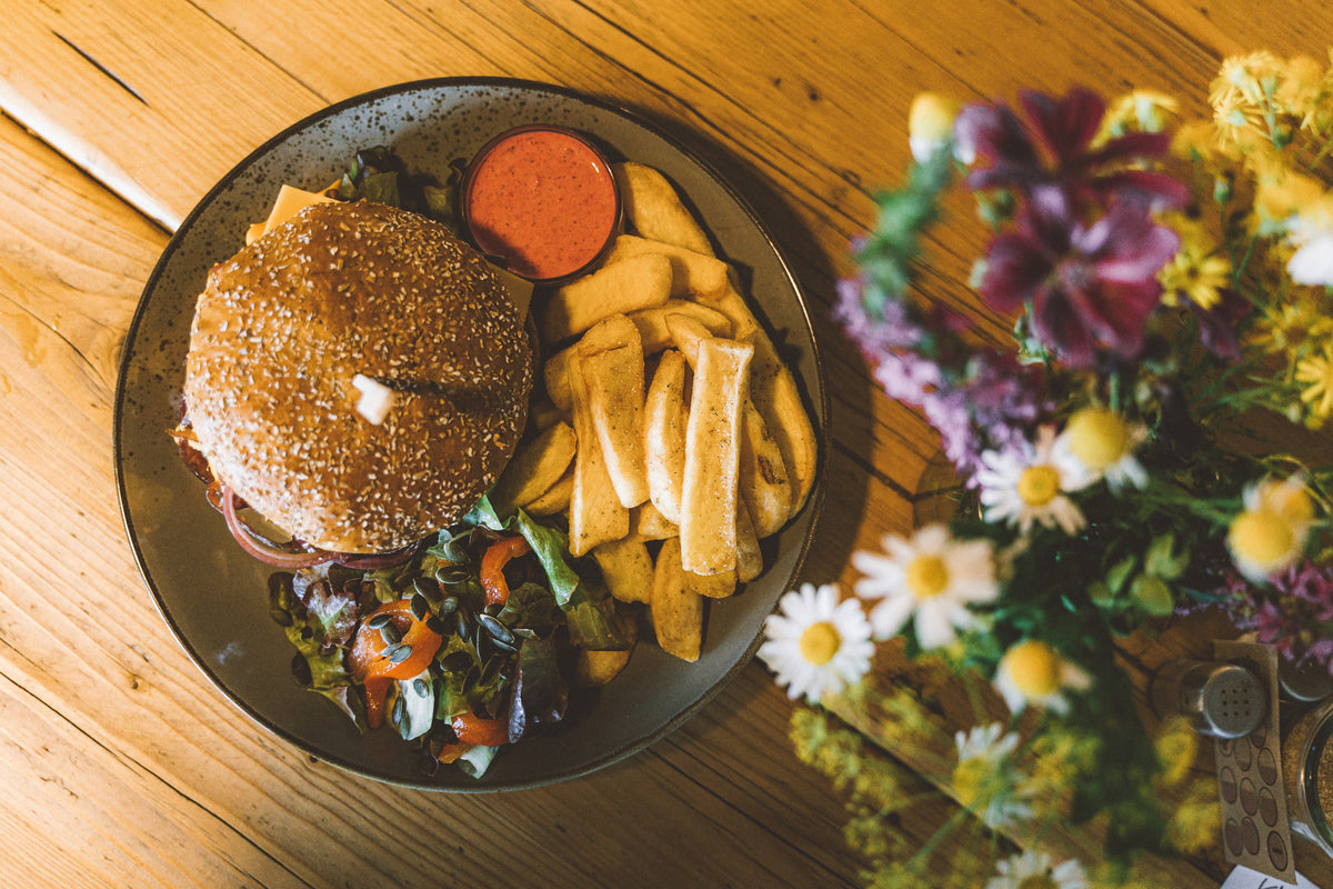 Burger mit Pommes und Salat, daneben ein Blumenstrauß