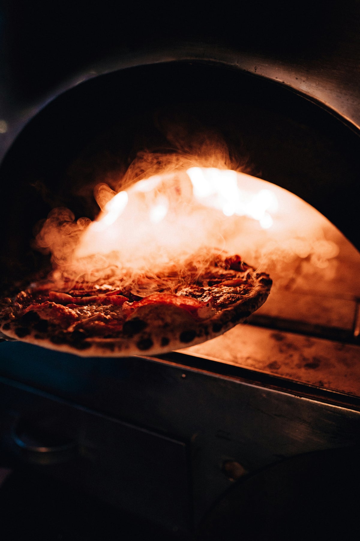 Pizza auf der Schaufel vor dem glühenden Ofen