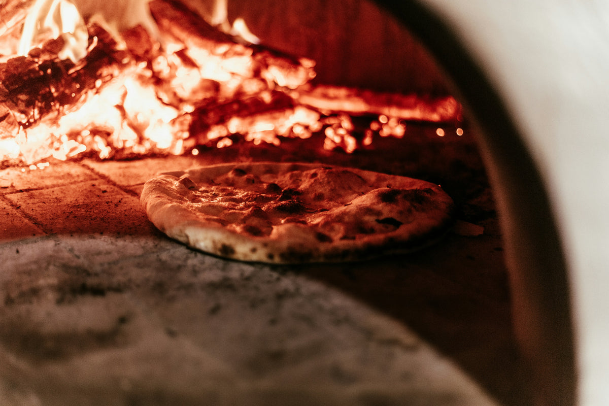 Pizza backt im Holzofen neben der Glut