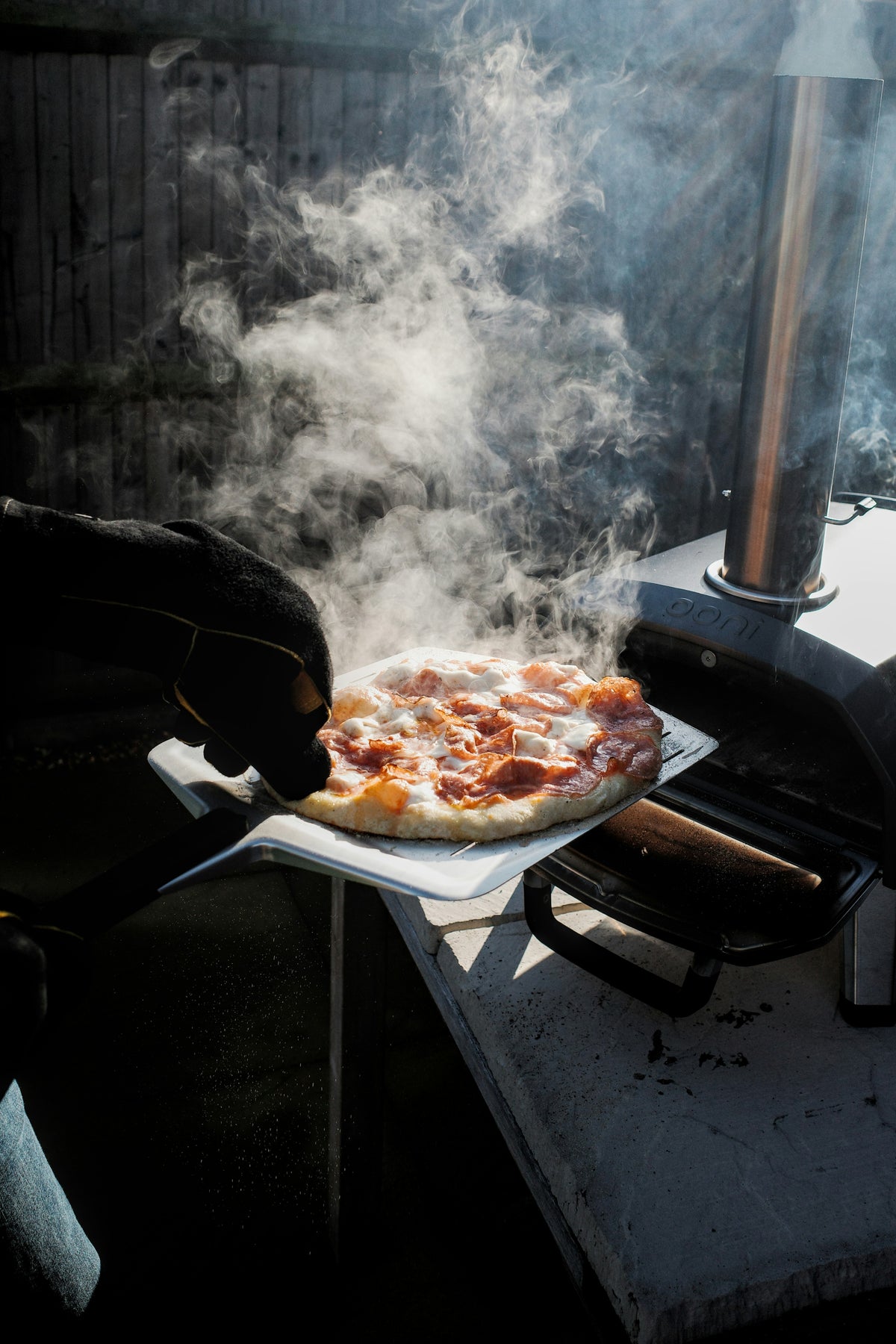 Pizza wird mit der Schaufel aus dem dampfenden Ofen geholt