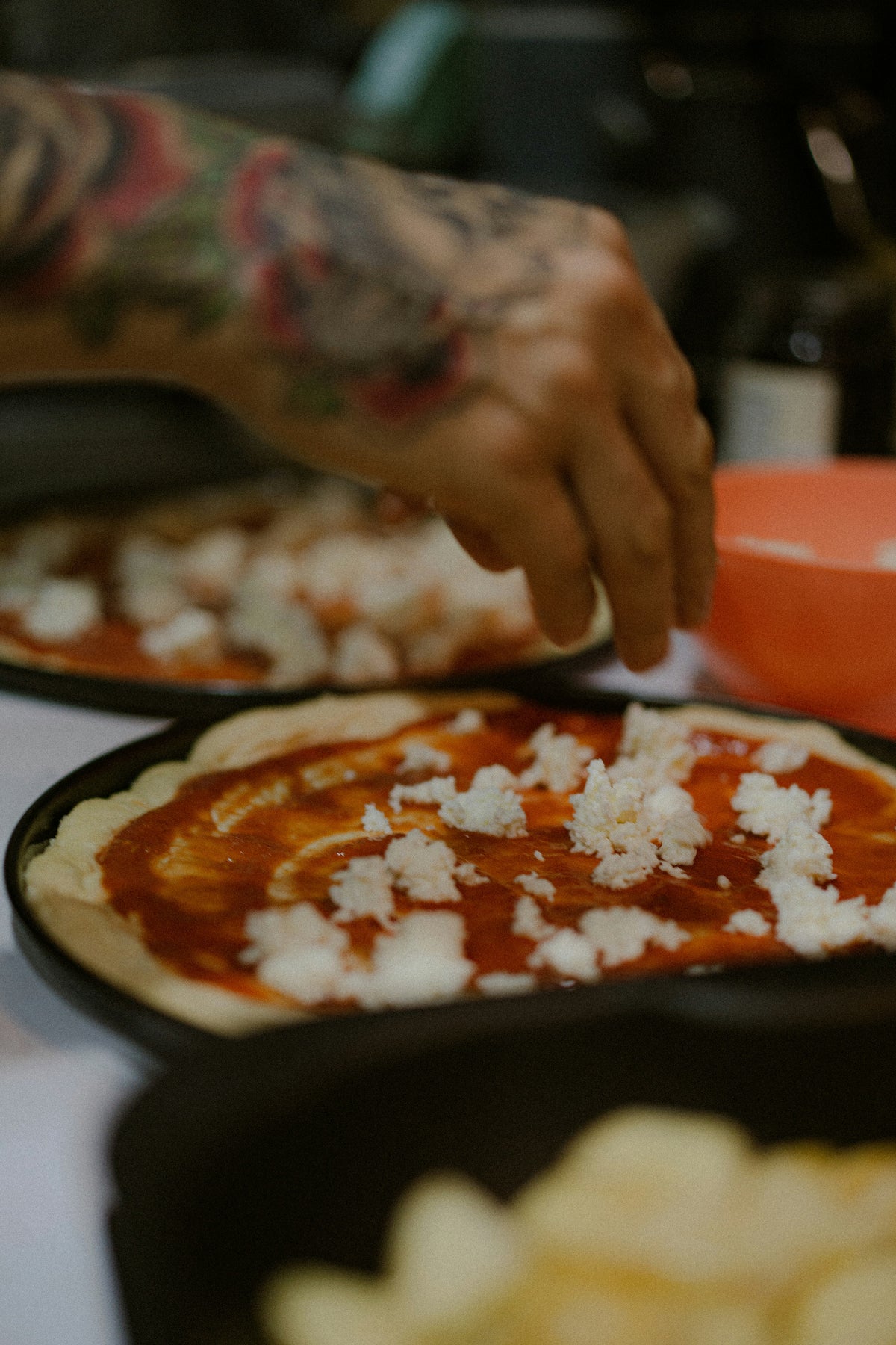 Hände belegen einen Pizzateig mit Tomatensoße und Mozzarella